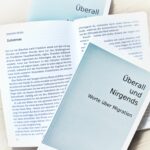Sammelband „Überall und Nirgends – Worte über Migration“ mit aufgeschlagenen Seiten des Beitrags „Zeitstrom“ von Johann Seidl.